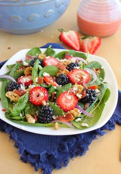 a white plate topped with berries and spinach salad next to a bowl of strawberries