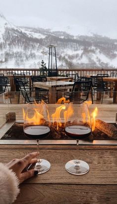 two people toasting wine glasses over an open fire pit with mountains in the background