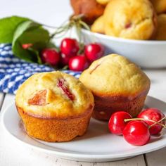 two muffins on a plate with cherries next to them