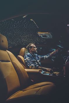 a man sitting in the driver's seat of a car with his hand on the steering wheel