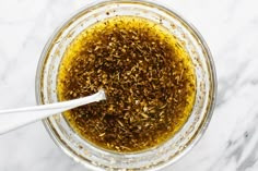 an overhead view of a bowl filled with olive oil and seasoning on a marble surface