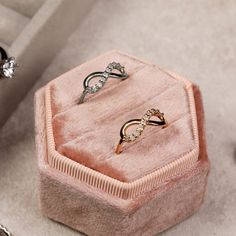 two rings are sitting in a pink velvet box on the floor next to other jewelry