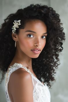 a woman with curly hair wearing a white dress and a flower in her hair is looking at the camera