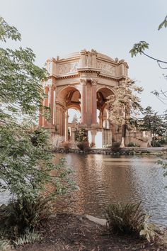 an old building sitting on the side of a lake next to some trees and bushes