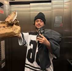 a man taking a selfie in an elevator holding a paper bag and cell phone