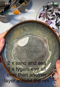 two hands are holding a bowl with the words 2x sand and sea 1x tygers eye all over them another layer around the rim