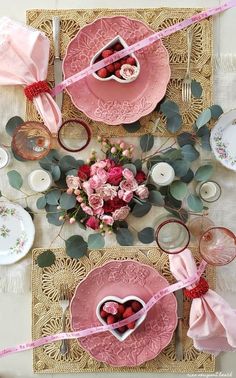 the table is set for valentine's day with pink plates and flowers on it