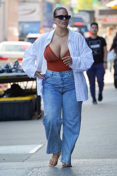 a woman walking down the street wearing high waisted jeans and a red bra top