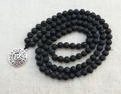 Mala made of 6mm Black Lava beads and OM pendant. This beautiful mala will be a pleasure to recite your mantras with, meditate with, or wear as a beautiful necklace. 108 beads (no knots). It measures approximately 26 inches in total length. Lava Stone is a grounding stone. It gives us strength and courage, allowing us stability through times of change. A calming stone, it is very useful in dissipating anger. Lava Stone enhances fertility. All our jewels arrive carefully packaged in a gift box re Om Pendant, 108 Mala Beads, Calming Stones, 108 Bead, Lava Bead, Mala Necklace, Lava Stone, Black Necklace, Mala Beads