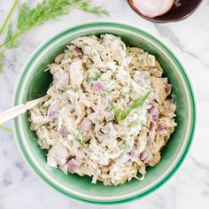 a green bowl filled with chicken salad next to a glass of wine on a marble table