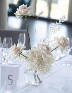 a vase filled with white flowers sitting on top of a table next to wine glasses