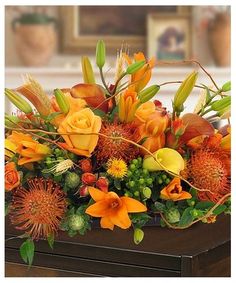 an arrangement of orange flowers and greenery on a table