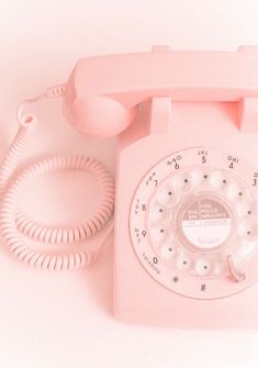 an old pink phone is sitting on a white surface and it's plugged in