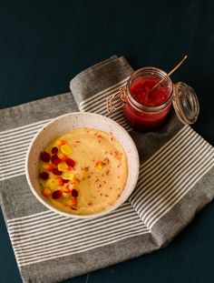 a bowl of food on a table next to a jar of jelly and a spoon