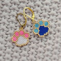 pair of earrings with blue, pink and white designs on them sitting on a knitted surface