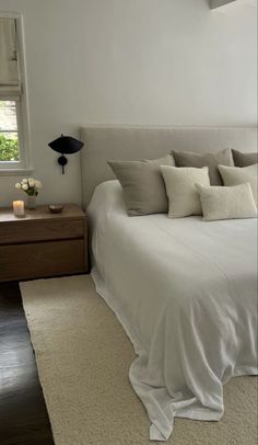 a white bed sitting under a window next to a night stand with candles on it