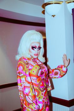 a woman with white hair and makeup is posing for the camera in a brightly colored outfit