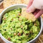 a person dipping guacamole into a bowl with crackers on the side