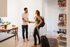 a man and woman are standing in the living room talking to each other while holding luggage