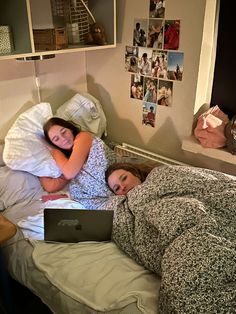 two women laying in bed with their arms around each other while looking at a laptop