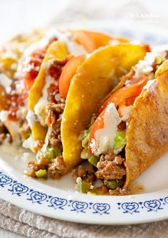 two tacos on a plate with meat, cheese and vegetables in the middle one is cut in half