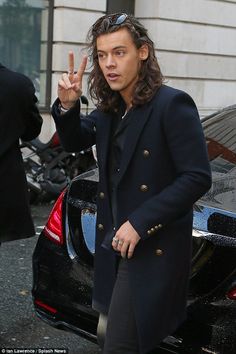 a man with long hair is standing in front of a car and giving the peace sign