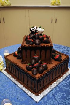 a triple layer chocolate cake with strawberries and chocolate frosting on top, sitting on a blue tablecloth