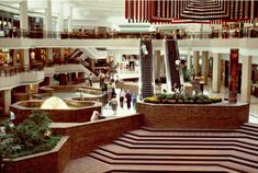 people are walking around in the lobby of a shopping mall with escalators and stairs