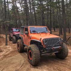 two jeeps driving down a dirt road in the woods