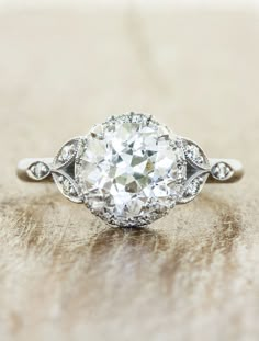 an old - fashioned diamond engagement ring sits on a wooden surface