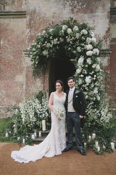 a bride and groom standing in front of an archway with white flowers on the side