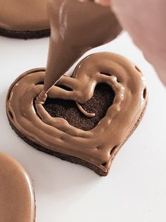 someone is decorating a heart shaped chocolate cookie with icing on the top and bottom