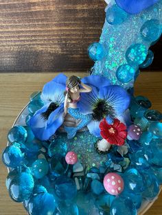 there is a cake decorated with blue and pink flowers on the plate, which has a fairy figurine in it