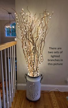 a vase with branches and lights in it on the floor next to a banister