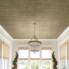 a chandelier hanging from the ceiling in a dining room with windows and chairs