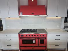 a red stove top oven sitting inside of a kitchen next to white cabinets and drawers