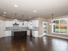 an empty kitchen and living room in a house with hard wood flooring, white cabinets and windows