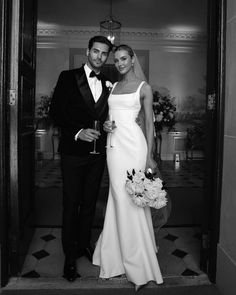 a man and woman in formal wear posing for the camera while holding champagne flutes together