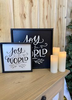 some candles are sitting on a table next to two framed signs that say joy, joy and word