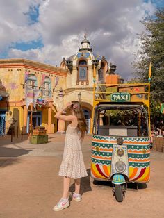 a woman is standing in front of a colorful bus at an amusement park while looking into the distance