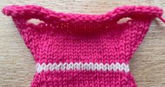 a pink and white knitted bag on top of a wooden table next to a pair of scissors