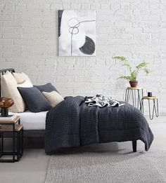 a bedroom with white brick walls and grey bedding, black and white decor on the wall