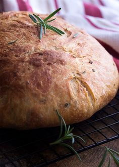 a loaf of bread with rosemary sprigs on top sitting on a cooling rack