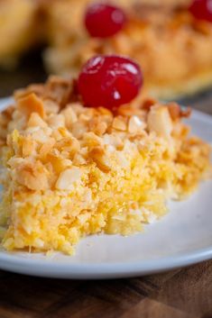 a piece of cake on a white plate with a cherry on top and another slice in the background