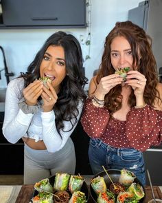 two women sitting at a table with food in front of their mouths and one holding her mouth open