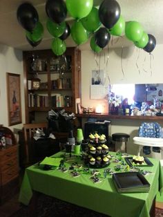 a green table topped with lots of black and green balloons hanging from it's ceiling