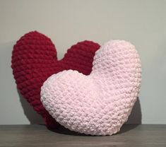 two crocheted heart shaped cushions sitting on top of a wooden table next to each other