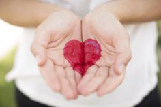 two hands holding a red heart in the palm