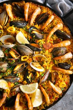 a pan filled with seafood and rice next to lemon wedges on top of a stove