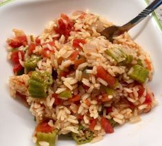 a white plate topped with rice and veggies next to a fork on a table